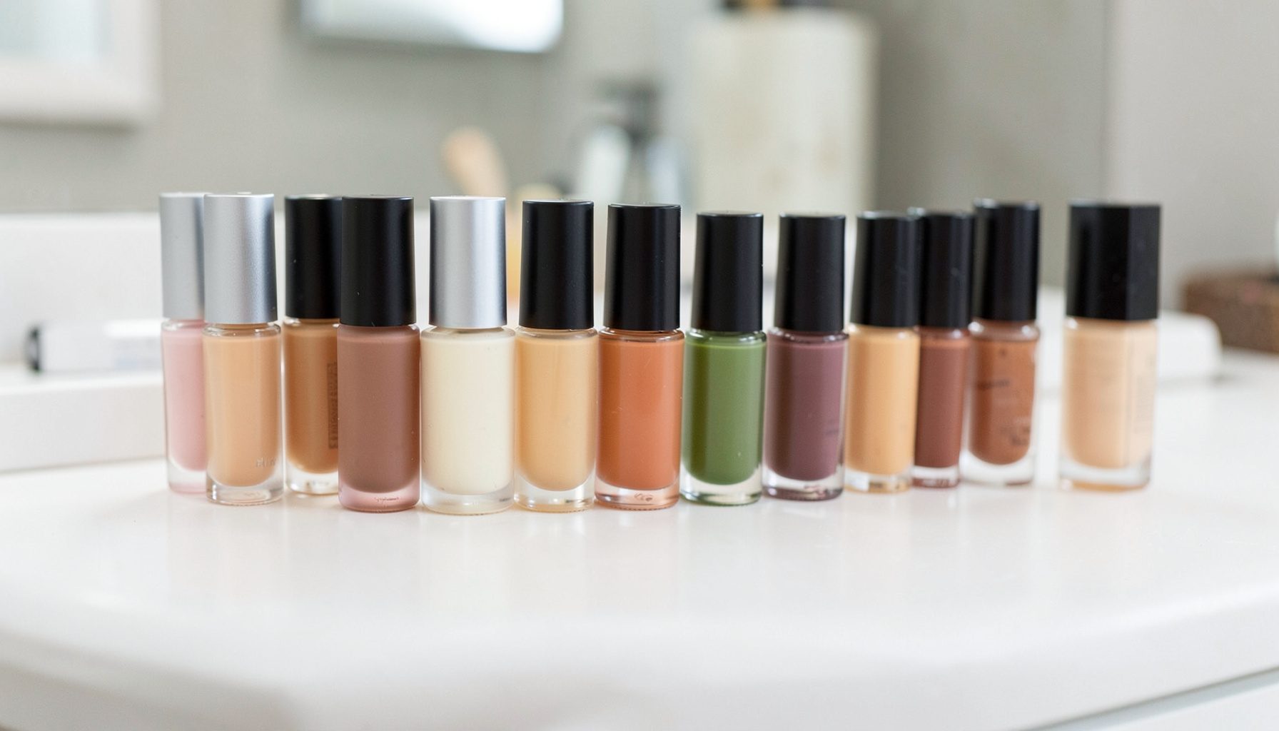 An array of liquid foundation bottles in varying shades lined up on a white vanity