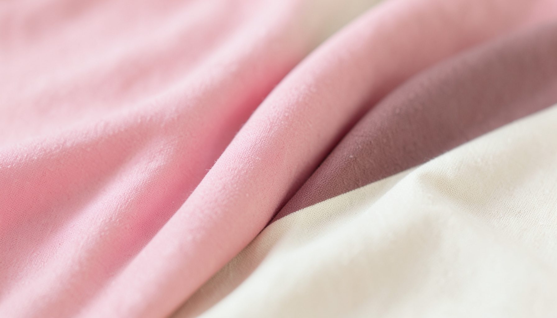 Soft pastel fabric textures in blush pink, dusty rose, and cream, arranged in gentle folds with a dreamy shallow depth of field